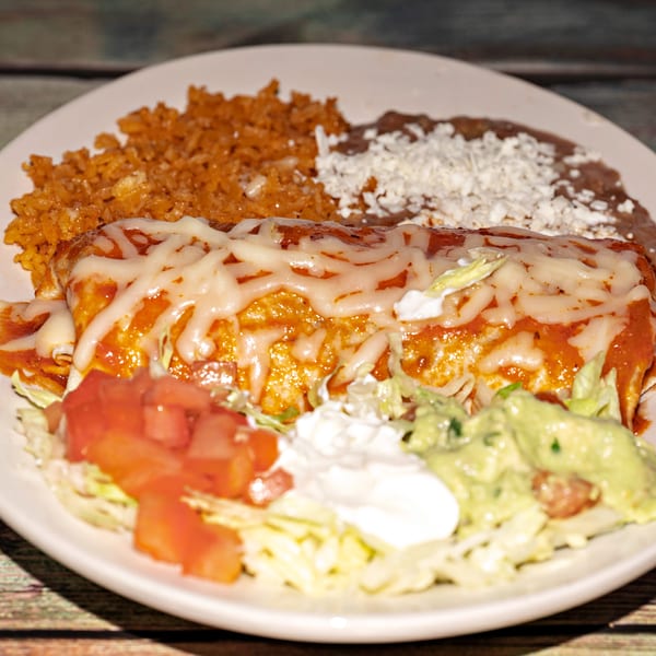 A cheese-covered burrito with rice, refried beans, lettuce, tomatoes, sour cream, and guacamole.