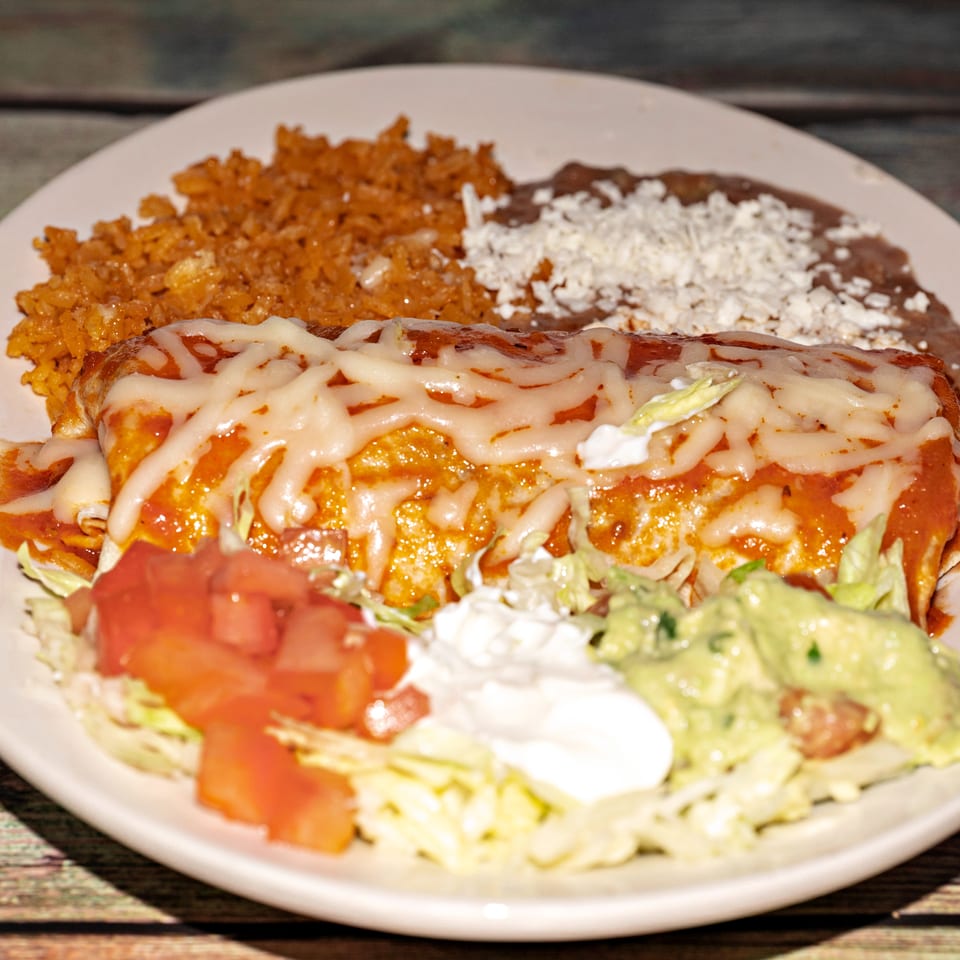 A cheese-covered burrito with rice, refried beans, lettuce, tomatoes, sour cream, and guacamole.