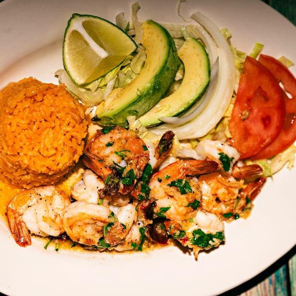 A plate of shrimp scampi with rice, sliced avocado, lime, and tomatoes.