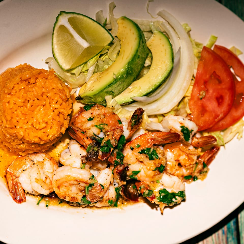 A plate of shrimp scampi with rice, sliced avocado, lime, and tomatoes.