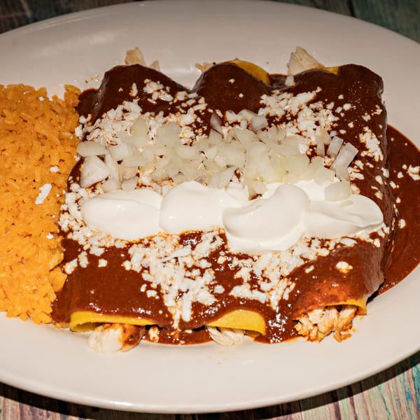 Chicken enchiladas with mole sauce, rice, cotija cheese, diced onions, and sour cream.